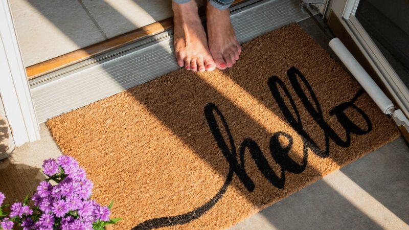 Frau barfuß vor der Haustür oder im neuen Zuhause mit schöner Fußmatte auf dem Boden