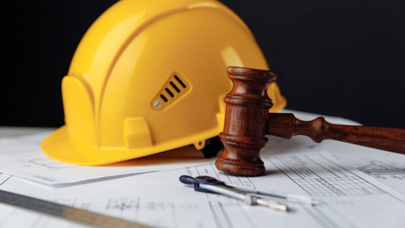 Holzhammer, Richterhammer mit gelbem Bauarbeiter-Helm, als Zeichen für Arbeitsrecht