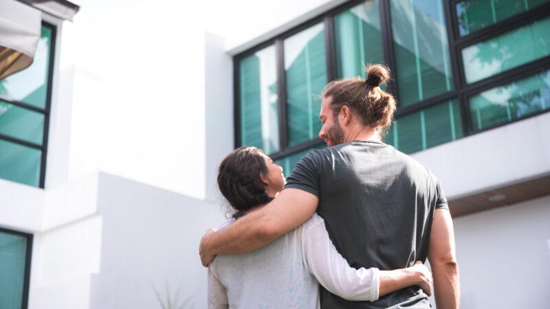 Paar, das vor einem neuen Haus steht und sich zusammen umarmt, Symbol für Hauskauf und Eigentum.
